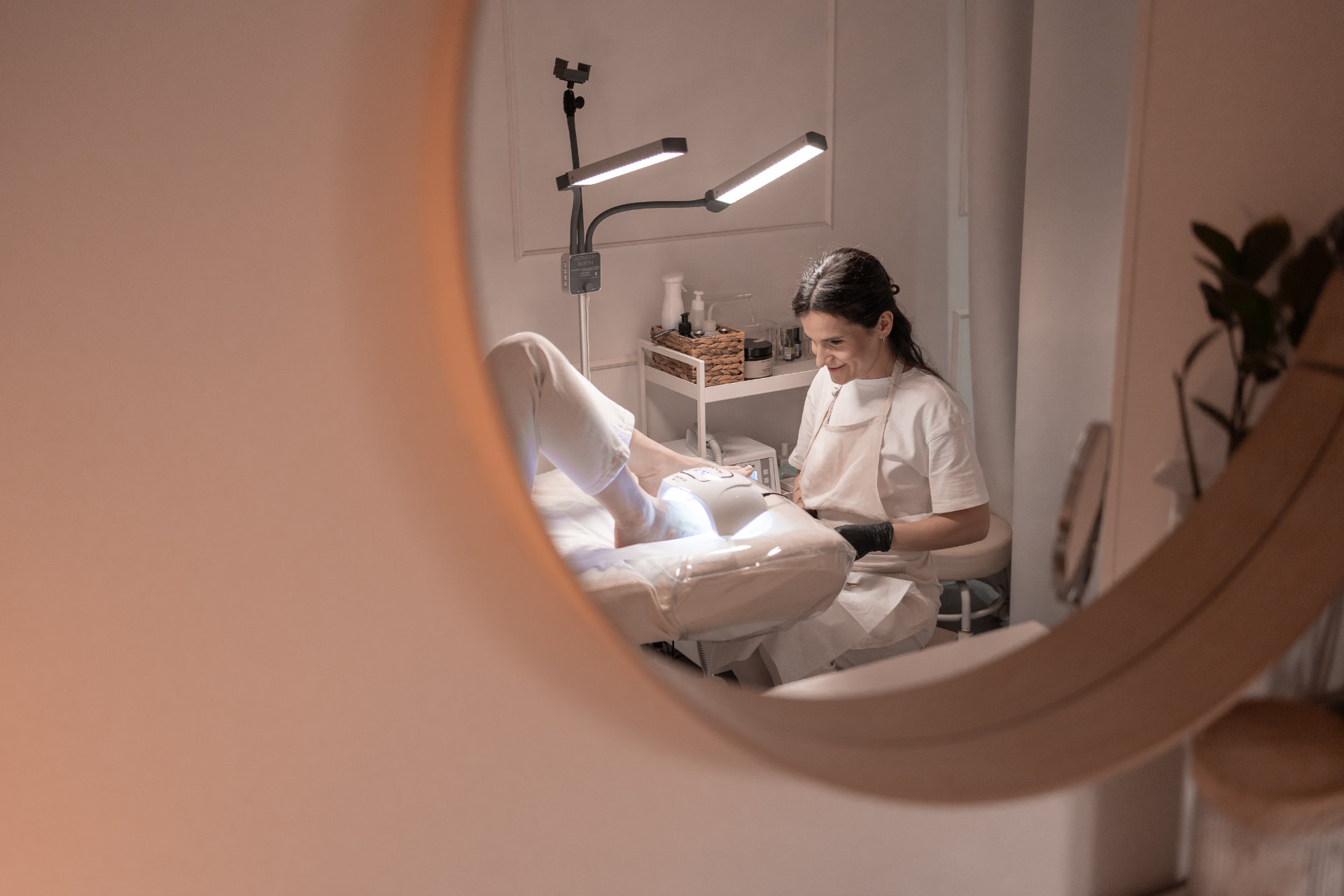 Pedicure hybrydowy w SKiN Białystok — stylistka utwardza lakier hybrydowy na stopach klientki w lampie UV